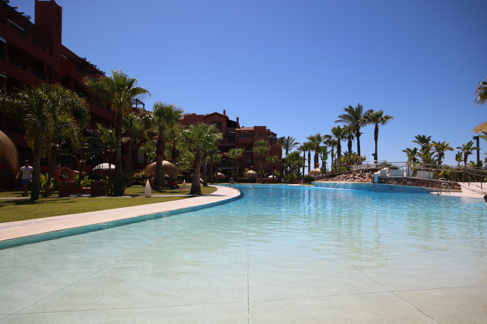 Beach-entry pool with waterfall spillover and palm landscaping